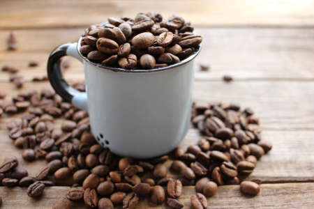 Cup of coffee beans on a wooden table. Close-up of coffee beans in a brown ceramic cup on wood background with copy space. Rustic styleの写真素材
