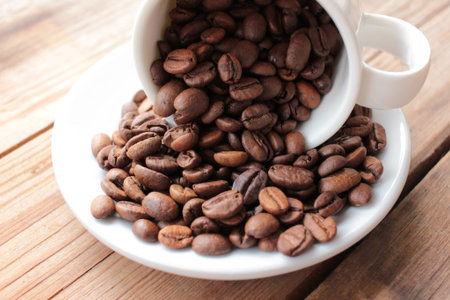 Cup of coffee beans on a wooden table. Close-up of scattered from a white ceramic cup coffee beans...