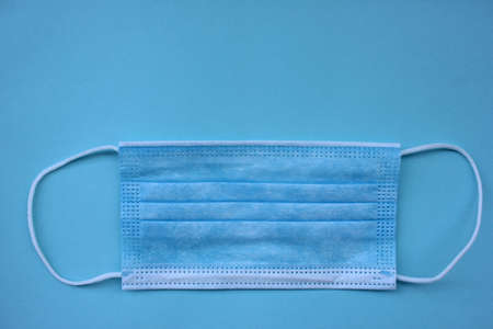 Disposable medical face mask on blue background with copy space. Pandemic protective face cover.の写真素材
