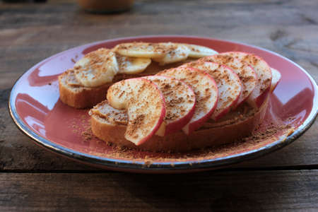 Breakfast with Peanut butter banana apple cinnamon sandwiches on wooden table. Slices of bread with peanut paste and fresh fruits on a plate. Healthy snacks for kids. Top view, selective focusの写真素材