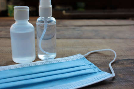 Disposable medical face mask and hand sanitizer bottles on wooden table background with copy space. Pandemic protective kit.の写真素材