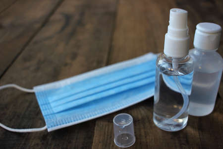 Disposable medical face mask and hand sanitizer bottles on wooden table background with copy space. Pandemic protective kit.の写真素材