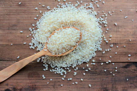 Wooden spoon with raw rice on wooden table background. Top view, copy space, selective focusの写真素材