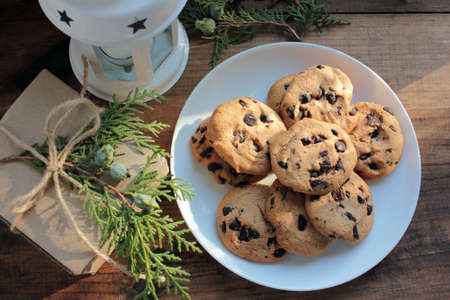 Homemade Christmas chocolate chip cookies, craft gift box decorated with evergreen twigs, and Christmas lantern on wooden background.の写真素材