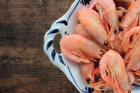 Cooked pink shrimps in the dish. Shell-on North Atlantic prawns in the bowl on rustic wooden table....