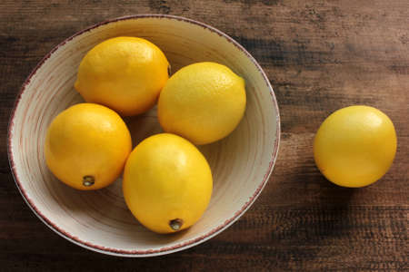Ripe yellow lemons in a bowl on wooden table. Flat lay, copy space. Rustic style compositionの写真素材