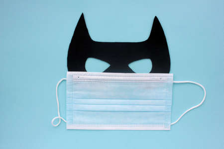 Bat Carnaval mask and covid medical face mask on blue background. Top view. Safe Christmas celebration conceptの写真素材