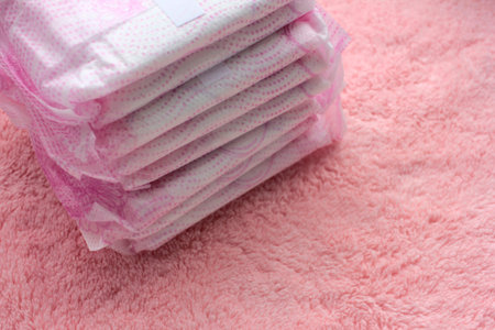 Stack of hygiene feminine menstruation pads on pink towel background. Close-up of protective...