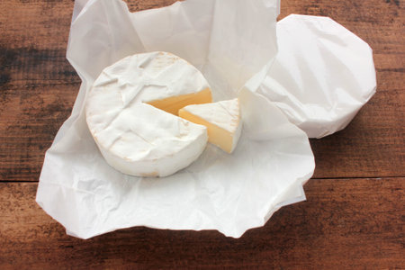 Camembert cheese on white packaging paper. Top view. Close up of white cheese on wooden background