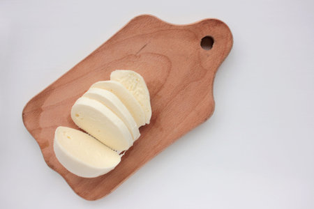 Sliced mozzarella cheese on cutting board on white table. Overhead view