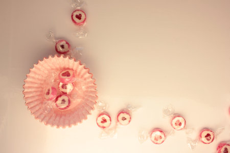 Overhead view of empty pink cupcake paper cups and round caramel candies with red hearst on white kitchen table. Holiday Valentines day background. Selective focusの写真素材