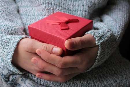 Woman hand in gray knitted sweater holding a red gift box. Valentines day present concept