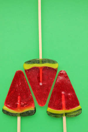Watermelon ice creams on green colored backdrop. Bright summer background. Lollipop in piece of watermelon shape. Candy on a stick. Top view, copy spaceの写真素材