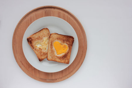 Toast bread with frighten egg in a heart shaped hole on plate on white background. Creative...