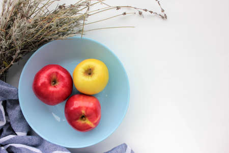 Red and green apple in blue bowl. Flat lay composition with fresh fruits, dry lavender flowers, and striped gray cloth napkin on white table background. Copy space, overhead viewの写真素材