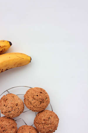 Oatmeal banana cookies on white table. Overhead view of oat biscuits and yellow fruits on white background with copy spaceの写真素材