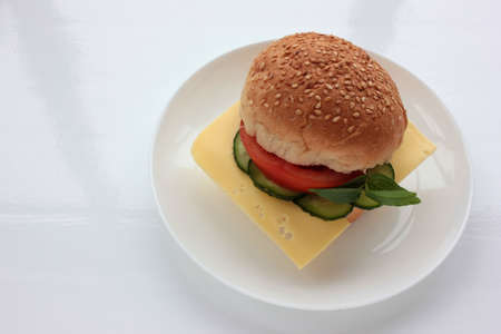 Cheese burger with tomato, cucumber and greens on white background. Healthy fast food. Sandwich with fresh vegetables.の写真素材