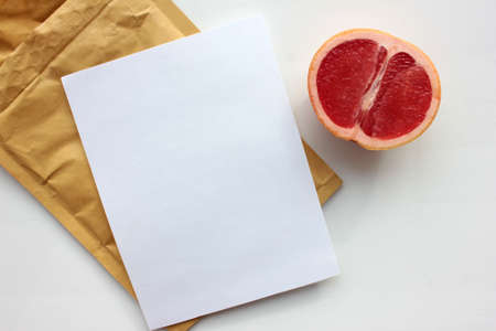 Summer still life with half of grapefruit, blank paper card and golden envelope on white background. Invitation mockup. Top view, copy space.の写真素材