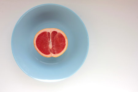 Half of grapefruit on a blue plate on a white background. Top view, copy space.の写真素材