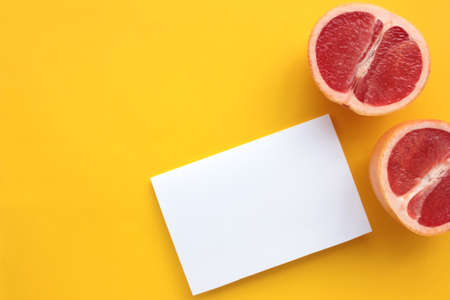 Summer still life with half of grapefruit and blank paper card.on yellow background. Invitation mockup on colored backdrop. Top view, copy spaceの写真素材