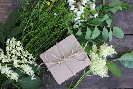 Brown craft gift box decorated with natural herbs and flowers on old wooden background with copy...
