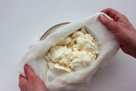 Old woman hands holding a homemade cottage cheese in cloth on white background. Ricotta cheese making process. Top view.の写真素材