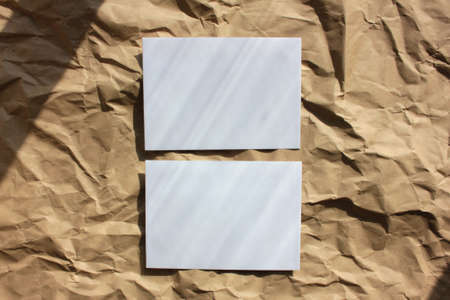 Blank white paper card or envelope on crumpled kraft paper background. Mock up invitation. Flat lay composition. Top view, copy space. Hard light, shadowの写真素材