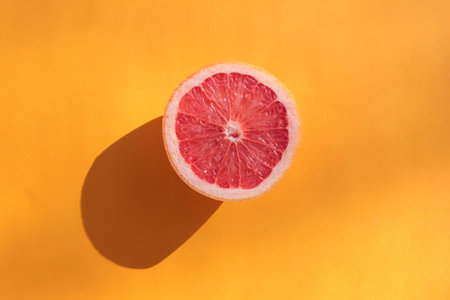Half of ripe grapefruit on orange background. Flat lay food composition with bright citrus fruit on...