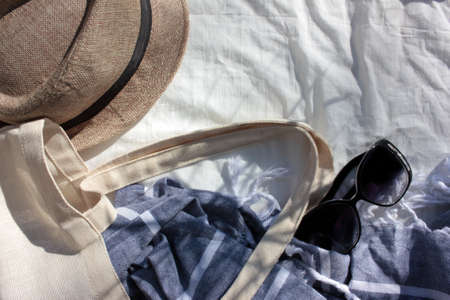 Summer flat lay with beach stuff on white fabric background. Season composition with sunglasses, hat, beach bag and towel. Top view, copy spaceの写真素材