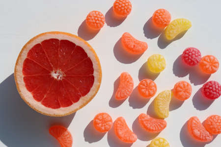 Slice of grapefruit and sweet fruit hard candies on white table background. Overhead view of colorful caramel mix. Hard light, shadow. Copy spaceの写真素材