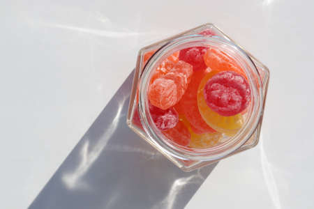 Sweet fruit hard candies in the glass mason jar on white table background. Overhead view of colorful caramel mix. Hard light, shadow. Copy spaceの写真素材