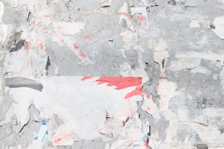 Ragged white and red posters on gray board background. Old bilboard with peeled placard. Crumpled...