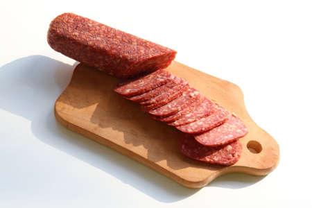 Slices of salami pepperoni on wooden cut board on white background. Top view, copy spaceの写真素材