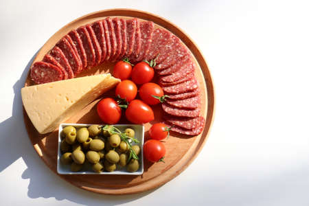 Salami cheese board with tomatoes and green olives on white table background. Set of appetizers. Flat lay food. Top view, copy spaceの写真素材