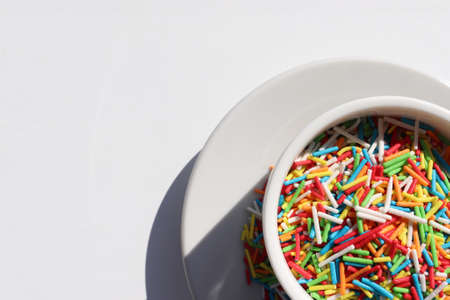 Rainbow sugar sprinkle dots, decoration for cake and bakery in coffee cup on white table. Colorful sprinkles easter background. Confectionery multicolored decorative topping. Top view, copy spaceの写真素材