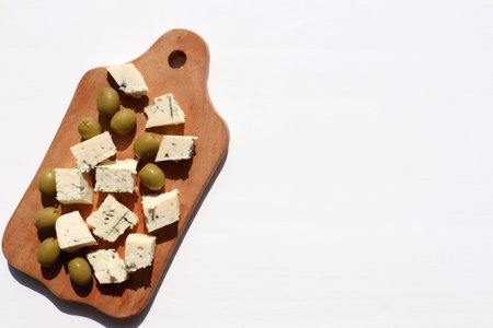 Sliced piece of blue cheese and green olives on wooden board background. Top view, close-up