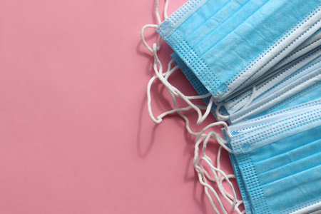 Stack of blue medical hygienic mask on colored backdrop. Protective pandemic face masks on pink...