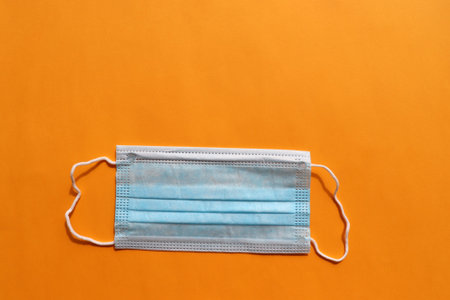 Stack of blue medical hygienic mask on colored backdrop. Protective pandemic face masks on yellow...