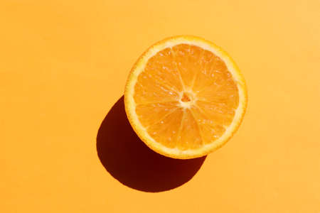 Half of orange on yellow background. Citrus fruit slice on colored backdrop. Top view, copy space. Summer tropical background. Hard light, shadowの写真素材