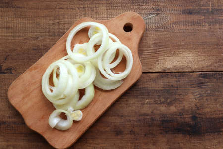 Raw onion rings on wood cutting board on wooden background. Top view, copy spaceの写真素材