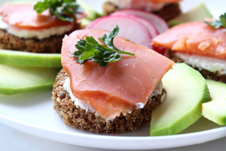 Smoked salmon avocado canapes on rye bread with cream cheese and parsley on plate. Sandwich with...