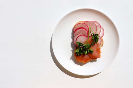 Sandwich with smoked salmon, radish, cream cheese, and parsley on white bread. Plate with healthy toast for breakfast on plate on white background. Top view, copy spaceの写真素材