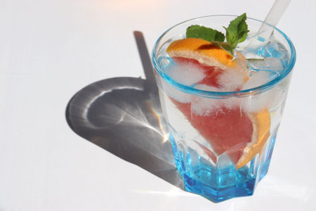 Summer cocktail with grapefruit and mint on white background. Refreshing drink with ice cubes. Glass...