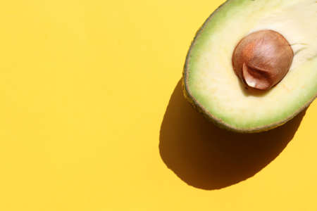 Avocado cut in half on colored yellow background. Top view, copy space. Hard light, shadowの写真素材