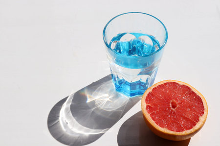 Summer still life with blue glass of cold water and half of grapefruit on white table background....