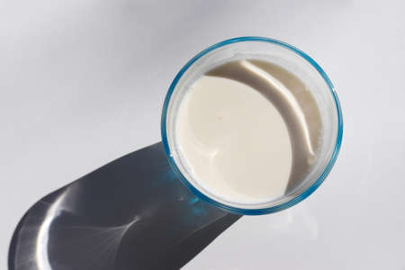 Glass of fresh organic milk on white table background. Top view, copy space. Hard light, shadowの写真素材