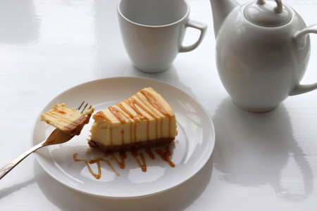 Piece of new york baked cheesecake with caramel sauce on plate on white table background. Close-up of cheese cake with topping. Top viewの写真素材