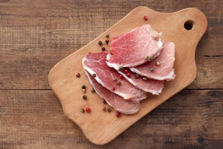 Raw pork chops on cutting board. Uncooked meat steaks for grilling with spices, pepper, salt and greens on wooden background. Top viewの写真素材