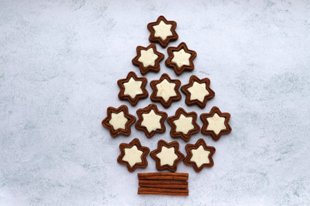 Christmas tree made of star-shaped cookies and cinnamon sticks on gray concrete background. Flat lay...