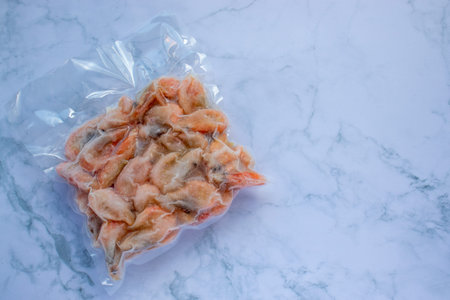 Frozen shrimps in vacuum transparent plastic packaging bag on white table background. Top view, copy...